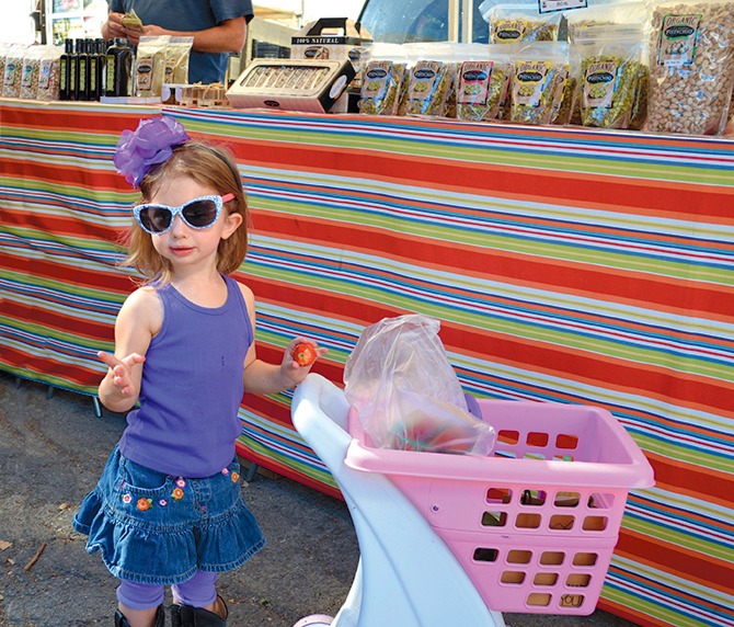 Zoey, a little girl, puts strawberries in a little pink cart. 