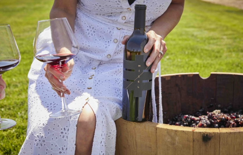 Woman sitting on wine barrel with wine bottle and glass